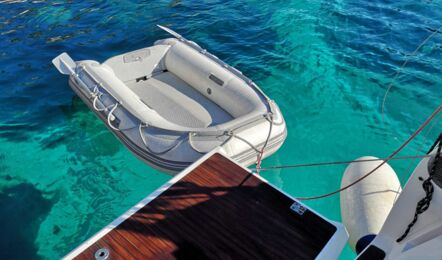 Blick von der Teak-Badeplattform der Bavaria cruiser 45 „Eva" über das Beiboot in einer türkisfarbenen Bucht – Yachtcharter